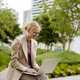 Woman works on laptop in city park during sunny day Woman works on laptop in city park during sunny day - PhotoDune Item for Sale