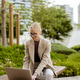 Woman works on laptop in outdoor park surrounded by greenery and buildings Woman works on laptop in outdoor park surrounded by greenery and buildings - PhotoDune Item for Sale