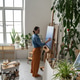 Creative female artist painting picture on canvas at home workshop surrounded by green plants. Creative female artist painting picture on canvas at home workshop surrounded by green plants. - PhotoDune Item for Sale