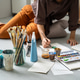Creative process at home art studio, talented woman painter drawing picture sitting on floor. Creative process at home art studio, talented woman painter drawing picture sitting on floor. - PhotoDune Item for Sale