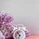 Alarm clock, lilac flowers and cup of coffee on light background. Alarm clock, lilac flowers and cup of coffee on light background. - PhotoDune Item for Sale