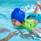 Smiling boy in a blue swim cap and green vest swims alongside a female instructor in a turquoise poo Smiling boy in a blue swim cap and green vest swims alongside a female instructor in a turquoise poo - PhotoDune Item for Sale