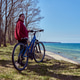 Young woman standing with bicycle near seaside under clear blue sky in sunny outdoor setting Young woman standing with bicycle near seaside under clear blue sky in sunny outdoor setting - PhotoDune Item for Sale