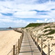 Wooden Boardwalk Curving Through Sand Dunes Toward the Ocean Under a Bright Blue Sky Wooden Boardwalk Curving Through Sand Dunes Toward the Ocean Under a Bright Blue Sky - PhotoDune Item for Sale