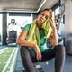 A woman sits down in the gym, taking a short break after an intense workout. A woman sits down in the gym, taking a short break after an intense workout. - PhotoDune Item for Sale