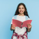 Smiling schoolgirl holding open notebook and looking at camera on studio background Smiling schoolgirl holding open notebook and looking at camera on studio background - PhotoDune Item for Sale
