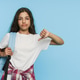 Displeased schoolgirl with backpack and books in hands showing thumbs down on blue studio background Displeased schoolgirl with backpack and books in hands showing thumbs down on blue studio background - PhotoDune Item for Sale