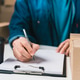Person Completing Shipping Documentation Beside Cardboard Package at Packing Workspace Person Completing Shipping Documentation Beside Cardboard Package at Packing Workspace - PhotoDune Item for Sale