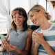 Women friends smiling and looking at a smartphone together while relaxing on a sunny terrace Women friends smiling and looking at a smartphone together while relaxing on a sunny terrace - PhotoDune Item for Sale