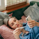 Woman at home checking temperature with digital thermometer while using a health app on smartphone Woman at home checking temperature with digital thermometer while using a health app on smartphone - PhotoDune Item for Sale