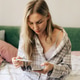 Woman at home checking thermometer and phone while sick in bed, concerned about fever and health Woman at home checking thermometer and phone while sick in bed, concerned about fever and health - PhotoDune Item for Sale