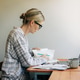 Woman working from home at a laptop sorting paperwork with coffee in a quiet home office Woman working from home at a laptop sorting paperwork with coffee in a quiet home office - PhotoDune Item for Sale