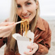 Blonde woman eating Asian takeout noodles with chopsticks from a box outdoors. Blonde woman eating Asian takeout noodles with chopsticks from a box outdoors. - PhotoDune Item for Sale