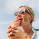 Woman enjoying a melting pink ice cream cone on a sunny day wearing sunglasses and a striped shirt Woman enjoying a melting pink ice cream cone on a sunny day wearing sunglasses and a striped shirt - PhotoDune Item for Sale