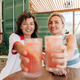 Two women smiling and toasting drinks together in a bright summer outdoor setting. Two women smiling and toasting drinks together in a bright summer outdoor setting. - PhotoDune Item for Sale
