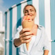 Smiling woman holds a melting strawberry ice cream cone toward the camera by a striped beach hut. Smiling woman holds a melting strawberry ice cream cone toward the camera by a striped beach hut. - PhotoDune Item for Sale
