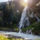 Mountain waterfall cascades rocky cliff fast river dense forest alpine landscape. Bright sunlight fl Mountain waterfall cascades rocky cliff fast river dense forest alpine landscape. Bright sunlight fl - PhotoDune Item for Sale