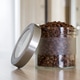 Glass jar of freshly roasted coffee beans on wooden table with natural light at home interior. Glass jar of freshly roasted coffee beans on wooden table with natural light at home interior. - PhotoDune Item for Sale
