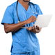 Medical worker uses laptop while smiling and stands in blue scrubs Medical worker uses laptop while smiling and stands in blue scrubs - PhotoDune Item for Sale