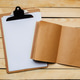 Writing tools on a wooden desk with a clipboard, blank paper, and a notebook Writing tools on a wooden desk with a clipboard, blank paper, and a notebook - PhotoDune Item for Sale