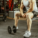 Man sits on a bench in gym and holds dumbbell during workout session at fitness center Man sits on a bench in gym and holds dumbbell during workout session at fitness center - PhotoDune Item for Sale