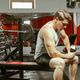 Man sits on bench in gym holding a container while resting his arm Man sits on bench in gym holding a container while resting his arm - PhotoDune Item for Sale