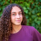 Young woman with curly brown hair and green eyes smiling, standing in front of green leaves Young woman with curly brown hair and green eyes smiling, standing in front of green leaves - PhotoDune Item for Sale