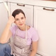 Woman relaxing in kitchen wearing apron and holding wooden spoon near oven Woman relaxing in kitchen wearing apron and holding wooden spoon near oven - PhotoDune Item for Sale