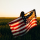 Young woman with American flag in a wheat field at sunset. 4th of July. Patriotic holiday. Young woman with American flag in a wheat field at sunset. 4th of July. Patriotic holiday. - PhotoDune Item for Sale