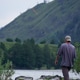 A fisherman with a fishing rod goes fishing on a mountain river, a view from behind the fisherman A fisherman with a fishing rod goes fishing on a mountain river, a view from behind the fisherman - PhotoDune Item for Sale
