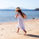Little girl in white dress playing on sunny beach with straw hat and ocean pier Little girl in white dress playing on sunny beach with straw hat and ocean pier - PhotoDune Item for Sale