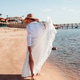 Woman in white dress walking along seaside beach with sun hat and flowing skirt Woman in white dress walking along seaside beach with sun hat and flowing skirt - PhotoDune Item for Sale