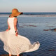 Woman in sun hat and white flowing skirt standing on shore at seaside vacation during summer Woman in sun hat and white flowing skirt standing on shore at seaside vacation during summer - PhotoDune Item for Sale