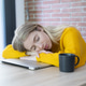 Young woman sleeping on a closed laptop at a table wearing a yellow sweater with a coffee mug nearby Young woman sleeping on a closed laptop at a table wearing a yellow sweater with a coffee mug nearby - PhotoDune Item for Sale