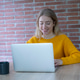 Smiling young woman working on a laptop at a wooden table with a coffee mug, wearing a yellow sweate Smiling young woman working on a laptop at a wooden table with a coffee mug, wearing a yellow sweate - PhotoDune Item for Sale