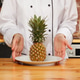 Chef presenting fresh pineapple on plate in kitchen. Chef presenting fresh pineapple on plate in kitchen. - PhotoDune Item for Sale