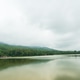 Calm lake reflecting a cloudy sky beside a lush green forest and misty hills Calm lake reflecting a cloudy sky beside a lush green forest and misty hills - PhotoDune Item for Sale