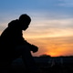 Silhouette of a man sitting by a campfire at sunset, reflecting in peaceful solitude Silhouette of a man sitting by a campfire at sunset, reflecting in peaceful solitude - PhotoDune Item for Sale
