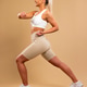 Athletic woman in white sports bra and beige leggings performing lunges in studio setting Athletic woman in white sports bra and beige leggings performing lunges in studio setting - PhotoDune Item for Sale