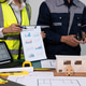Construction team reviewing building plans and charts at a worktable with laptop, blueprints, tools Construction team reviewing building plans and charts at a worktable with laptop, blueprints, tools - PhotoDune Item for Sale