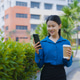 Asian businesswoman in blue shirt using smartphone and holding coffee paper cup at outdoor Asian businesswoman in blue shirt using smartphone and holding coffee paper cup at outdoor - PhotoDune Item for Sale
