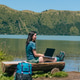 Young adult woman using laptop on a wooden bench beside a lake and mountains Young adult woman using laptop on a wooden bench beside a lake and mountains - PhotoDune Item for Sale