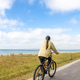 Woman cycling near the coast. Vertical seaside travel scene. Woman cycling near the coast. Vertical seaside travel scene. - PhotoDune Item for Sale