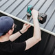 A young guy with a drill is screwing screws into the roof caps of a metal shed. A young guy with a drill is screwing screws into the roof caps of a metal shed. - PhotoDune Item for Sale