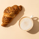 Coffee cup and croissant at colored background with sunny shadow. Coffee cup and croissant at colored background with sunny shadow. - PhotoDune Item for Sale