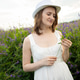 Woman in white dress and hat standing in flowery field. Girl holding purple wild flower during summe Woman in white dress and hat standing in flowery field. Girl holding purple wild flower during summe - PhotoDune Item for Sale