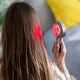 Woman using red light therapy device on hair in bedroom Woman using red light therapy device on hair in bedroom - PhotoDune Item for Sale