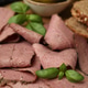 Slices of tasty pastrami (cured beef meat) and basil leaves on table, closeup Slices of tasty pastrami (cured beef meat) and basil leaves on table, closeup - PhotoDune Item for Sale