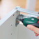 A woman using a compact cordless electric screwdriver to assemble white wooden furniture. A woman using a compact cordless electric screwdriver to assemble white wooden furniture. - PhotoDune Item for Sale