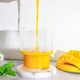 Pouring fresh mango smoothie into a glass on a white table with shadows. Pouring fresh mango smoothie into a glass on a white table with shadows. - PhotoDune Item for Sale